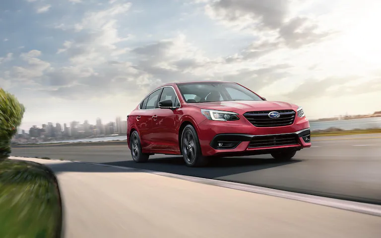 A 2022 Subaru Legacy driving on a road heading out of a city.